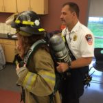 fire instructor strapping in student to firefighter unifiorm