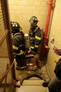 Two Columbus Firefighters, dressed in full turnout gear, drag a mannequin down a flight a stairs during a simulation exercise.  