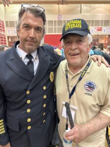 Columbus Fire Chief Andy Lay stands with an arm around Retired Fire Chief Larry McCord at a Indy Honor Flight reception held on Saturday April 15th, 2023. Chief Lay is Dresses in his Class A fire Deparment uniform. Chief McCord in dressed in his Indy Honor Flight Polo shirt and is wearing a Vietnam Veteran Ball Cap. 