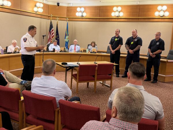 Board of Works Chammber is filled with City officials and Firefighters. Three Firefighters stand before the boardroom to accept commendations. The firefighters stand will little emotions on their faces as a chief officer in white recounts the events of the emergency call.
