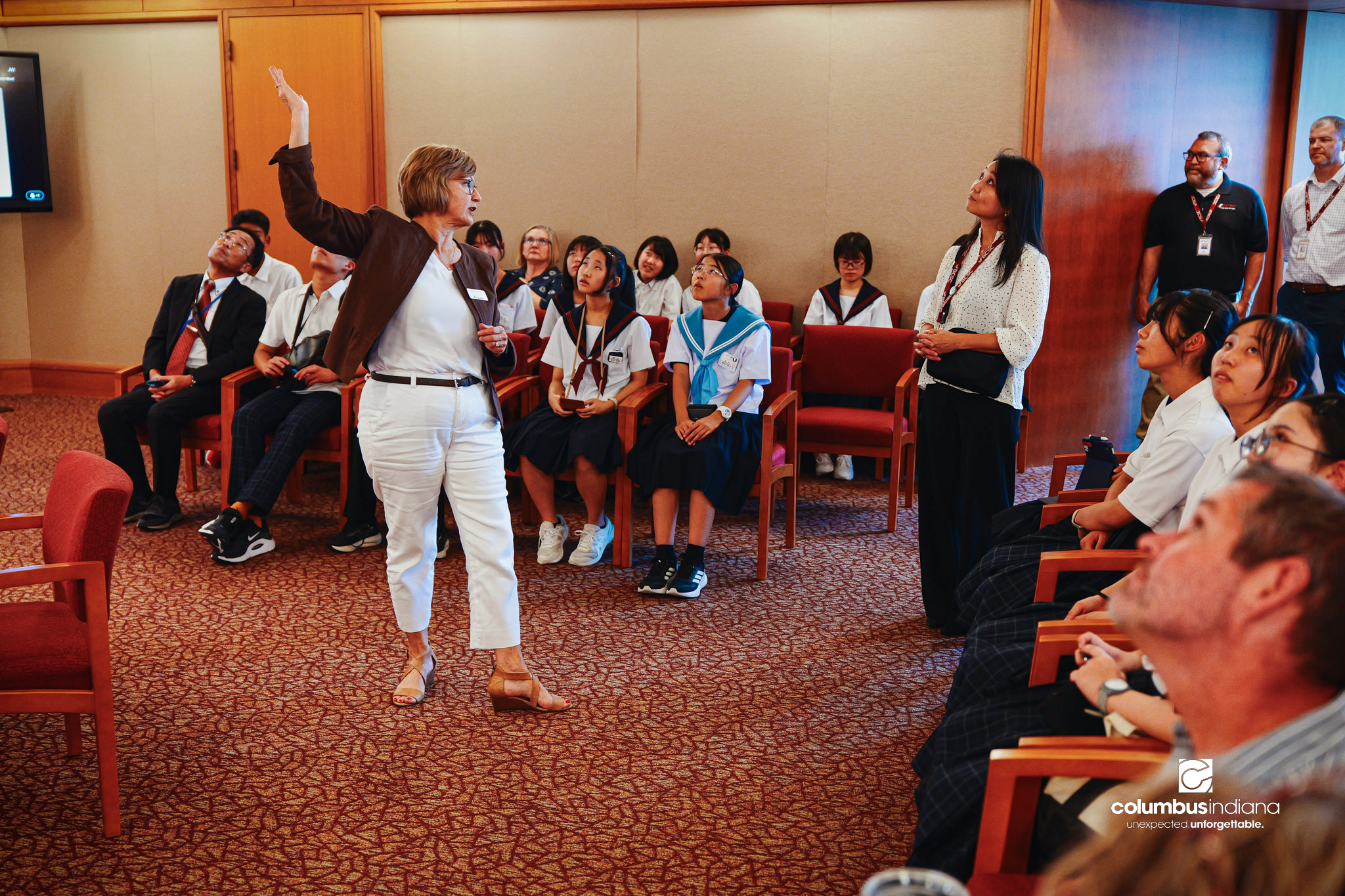 Nancy Wagner, executive assistant to the mayor, talks about the William T. Wiley History & Mystery of Columbus painting above council chambers to a delegation of students and school officials from Miyoshi-Minami Junior High School touring Columbus Ci