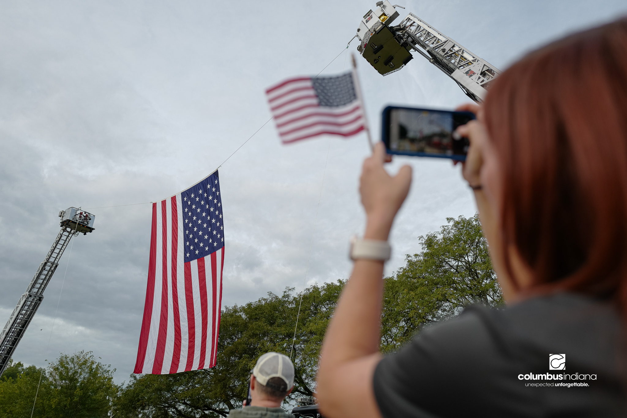 Spectators look on as a large American flag is raised before a ceremony to commemorate the 25th anniversary of Sept. 11, at Columbus City Hall in Columbus, Ind., Friday, Sept. 11, 2026.