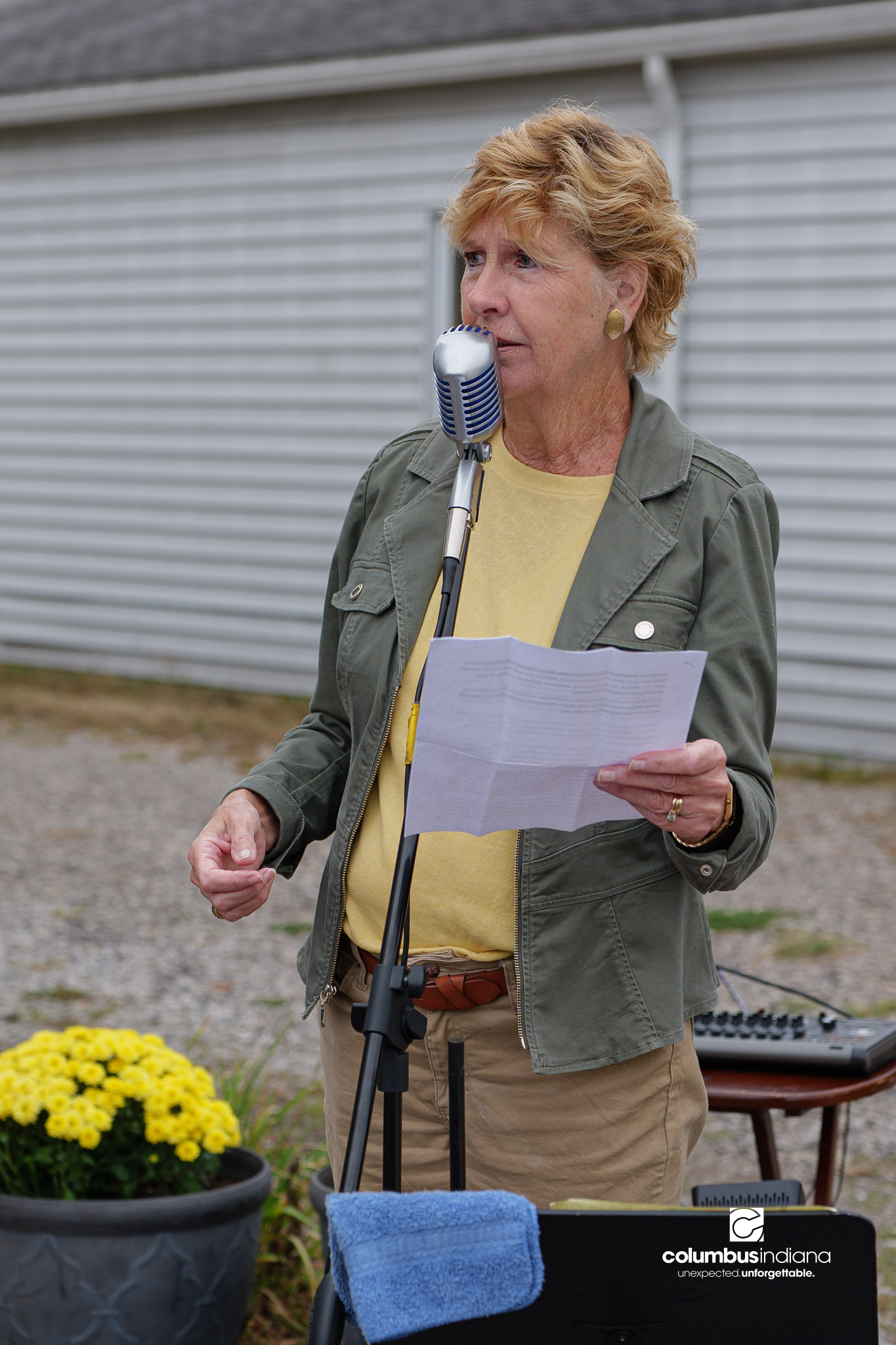 The mayor, a woman, stands at a mircrophoen giving a speech.